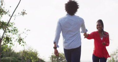 Happy african american couple walking together and holding hands on sunny day, slow motion. Lifestyle, countryside and nature concept.