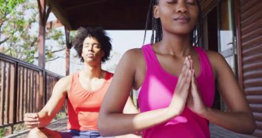 Mutlu Afro-Amerikan çifti yoga yapıyor ve kulübede meditasyon yapıyor, ağır çekimde. Yaşam tarzı, ev hayatı, kırsal ve doğa kavramı.