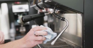 Hands of caucasian male barista cleaning coffee machine with cloth in cafe. Local business owner and hospitality concept.