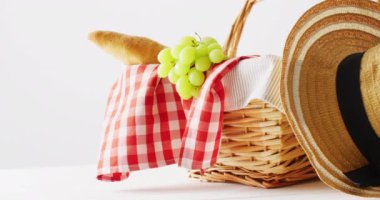 Picnic basket with checkered blanket, grapes, baguette and hat on white background with copy space. Picnic day, food and nature concept.