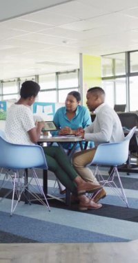 Vertical video of diverse business people sitting at table and talking in office. Global business and modern office concept.