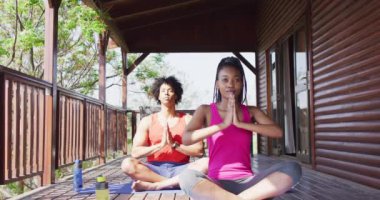 Mutlu Afro-Amerikan çifti yoga yapıyor ve kulübede meditasyon yapıyor, ağır çekimde. Yaşam tarzı, ev hayatı, kırsal ve doğa kavramı.