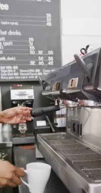 Vertical video of biracial female barista preparing coffee in coffee machine in cafe. Cafe, barista and business concept.