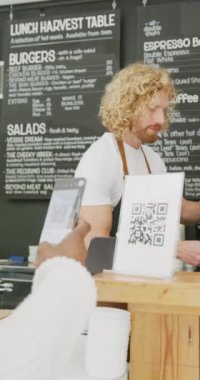 Kafedeki akıllı telefonla soru cevap kodunu tarayan mutlu erkek barista ve kadının dikey videosu. Kafe, kahveci ve iş konsepti.