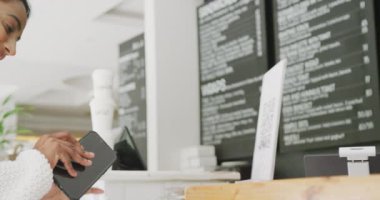 Happy biracial woman scanning qr code with smartphone in cafe. On the go, technology, local business and hospitality concept.