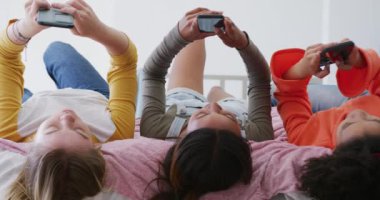 Yatakta uzanan ve akıllı telefonlar kullanan mutlu genç kızlar. Ağır çekimde. Arkadaşlar, eğlence, ev konseptinde kaliteli zaman geçirme..