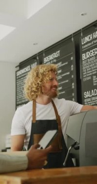 Kafede kahvesini akıllı telefondan ödeyen mutlu erkek ve kadının dikey videosu. Kafe, kahveci ve iş konsepti.