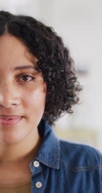Vertical video half face portrait of happy biracial woman at home smiling to camera, in slow motion. Free time, happiness and lifestyle concept.