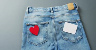 Close up of jeans with heart and white note on grey background with copy space. Denim day, material, style and design concept.