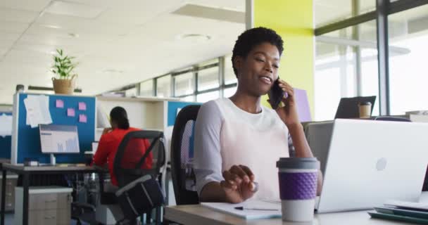 아프리카 미국인 사업가가 노트북을 사용하고 사무실에서 스마트폰으로 느리게 말하고 있습니다 — 비디오