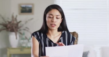 Asian woman making business video call at home, talking and gesturing, slow motion. Working from home, small business and lifestyle concept.