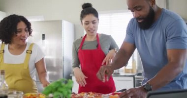 Gülümseyen çeşitli kadın ve erkek arkadaşlar pizza yapıyor ve mutfakta yavaş çekimde yemek pişiriyorlar. Aşçılık, arkadaşlık ve yaşam tarzı kavramı.