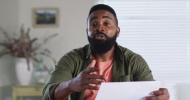 African american man making business video call at home, talking and gesturing, slow motion. Working from home, small business and lifestyle concept.