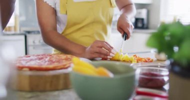 Smiling diverse female and male friends cooking and talking in kitchen, in slow motion. Cooking, friendship and lifestyle concept.