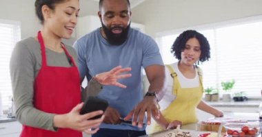 Smiling diverse female and male friends cooking and talking in kitchen, in slow motion. Cooking, friendship and lifestyle concept.