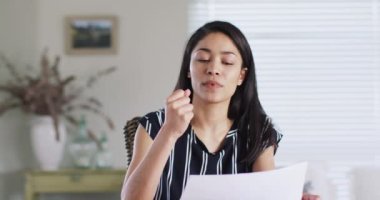 Asian woman making business video call at home, talking and gesturing, slow motion. Working from home, small business and lifestyle concept.