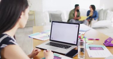 Asian woman making laptop video call, copy space on screen, colleagues behind, slow motion. Working from home, small business, friendship and lifestyle concept.