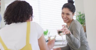 Happy diverse male and female friends drinking wine in kitchen, in slow motion. Friendship, cooking and lifestyle concept.