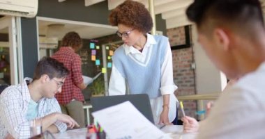 Diverse businesswoman standing and addressing male colleagues in casual meeting, slow motion. Start up business, teamwork, inclusivity and communication concept.