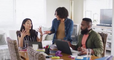 Diverse male and female friends using laptop and talking, working at home, in slow motion. Friendship, working from home and start up business concept.