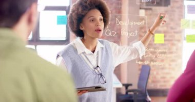 Biracial creative businesswoman with tablet in casual meeting with diverse colleagues, slow motion. Start up business, work, inclusivity and communication concept.