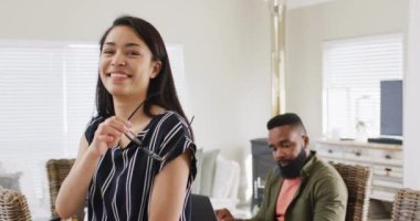 Smiling biracial woman and diverse female and male friends working at home, in slow motion. Friendship, working from home, small business and start up business concept.