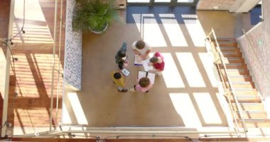 High angle of five diverse male and female colleagues in casual discussion in corridor, slow motion. Start up business, teamwork, inclusivity and communication concept.