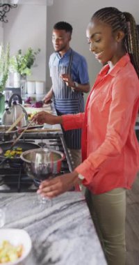 Vertical video of happy african american couple preparing meal together. Love, relationship, lifestyle and spending time together concept.