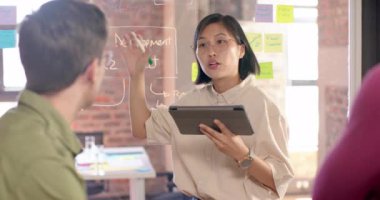 Asian creative businesswoman with tablet in casual meeting diverse colleagues, slow motion. Start up business, work, inclusivity and communication concept.