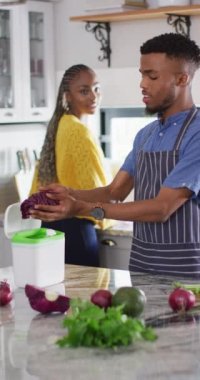 Vertical video of happy african american couple preparing meal together. Lifestyle, spending free time at home concept.