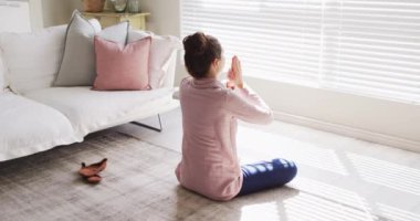 Caucasian woman sitting on floor, practicing yoga and meditating in living room. Spending quality time at home concept.