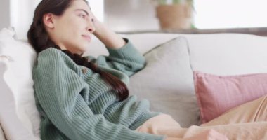 Happy caucasian woman sitting on couch and stretching in living room. Spending quality time at home concept.