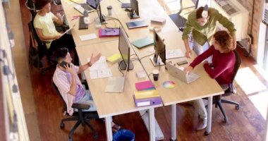 High angle of diverse female and male creative colleagues at work in casual office, slow motion. Start up business, teamwork, inclusivity and communication concept.