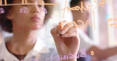 Biracial creative businesswoman brainstorming ideas, writing on glass wall, slow motion. Start up business, work and communication concept.