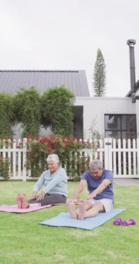 Vertical video of happy senior biracial couple practicing yoga in garden. Spending quality time at home, retirement and lifestyle concept.