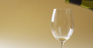 White wine pouring into glass over yellow background with copy space. Wine, alcohol, beverage and wine tasting concept.