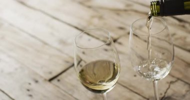 White wine pouring into glasses over wooden surface with copy space. Wine, alcohol, beverage and wine tasting concept.