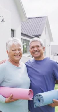 Vertical video of portrait of happy senior biracial couple with yoga mats in garden. Spending quality time at home, retirement and lifestyle concept.