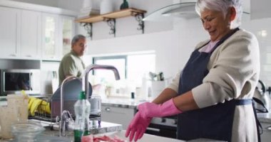 Happy senior biracial couple washing dishes in kitchen. Spending quality time at home, retirement and lifestyle concept.