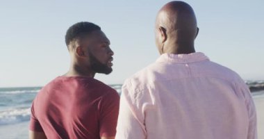 Video of african american senior father and adult son walking on beach and talking. Holidays, vacations, relations and spending quality family time together concept.