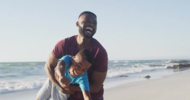 Video of happy african american father and son having fun on beach. Holidays, vacations, relations and spending quality family time together concept.