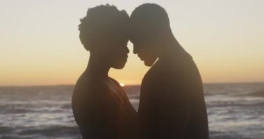 Mutlu Afro-Amerikan çiftlerin gün batımında sahilde kucaklaşmalarını gösteren bir video. Tatiller, tatiller, rahatlamak ve ailece sahilde güzel vakit geçirmek..