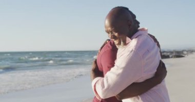 Video of african american senior father and adult son embracing on beach. Holidays, vacations, relations and spending quality family time together concept.