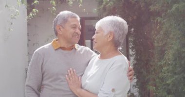 Portrait of happy senior diverse couple looking at camera in garden. Spending quality time at home, retirement and lifestyle concept.