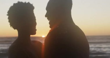 Video of happy african american couple embracing on beach at sunset. Holidays, vacations, relax and spending quality family time on beach.