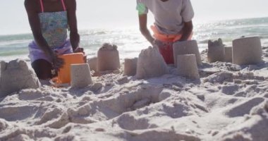 Video of happy african american kids playing with sand on beach. Holidays, vacations, relax and spending quality family time together concept.
