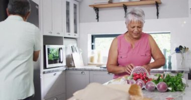 Happy senior biracial couple holding vegetables in kitchen. Spending quality time at home, retirement and lifestyle concept.