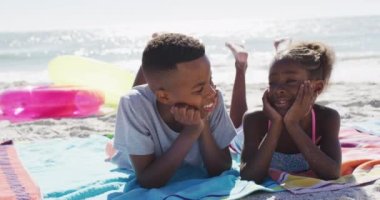 Video of happy african american sibling lying on towel on beach. Holidays, vacations, relax and spending quality family time together concept.