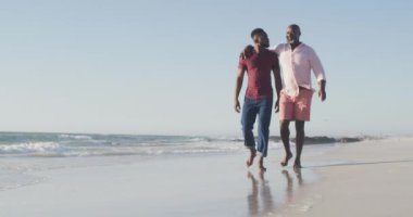 Video of happy african american senior father and adult son walking on beach. Holidays, vacations, relations and spending quality family time together concept.