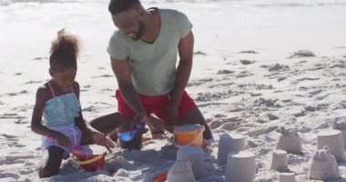 Video of happy african american father and daughter playing with toys on beach. Holidays, vacations, relax and spending quality family time together concept.